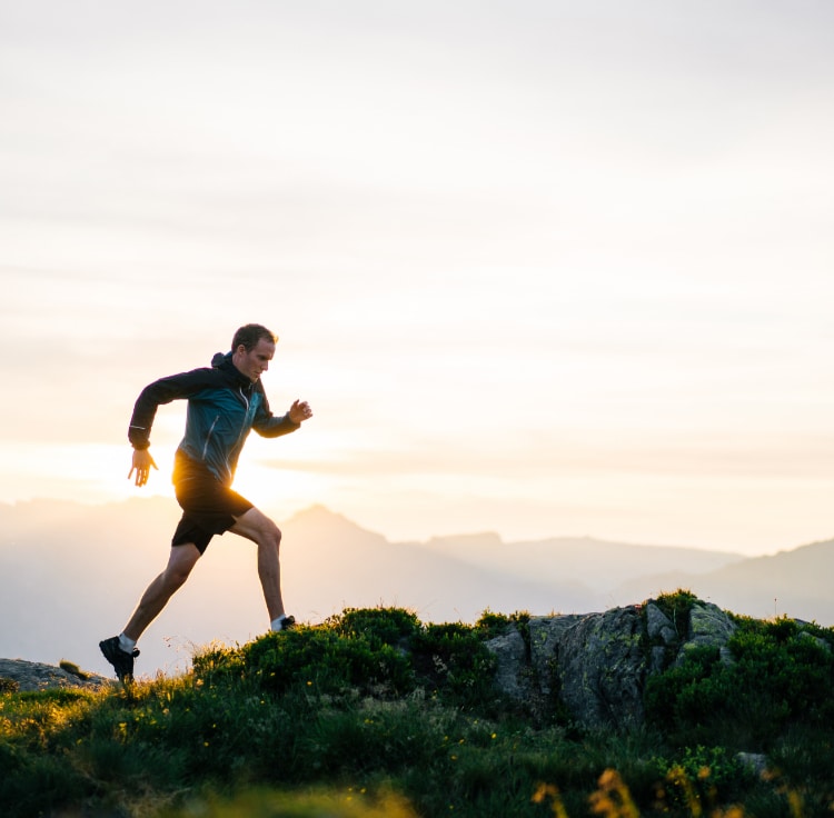 man running across a mountain top with other mountains in the background